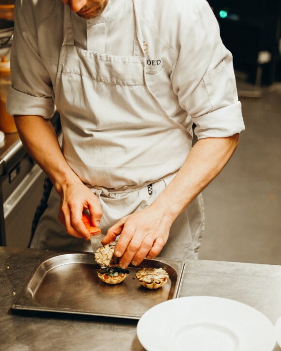 Michaël Vrijmoed in his restaurant serving two plates, with glasses of champagne and a bottle of La Grande Dame 2015